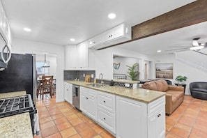 A modern kitchen with white cabinetry, a granite countertop, and a dining area with a wooden table and chairs.