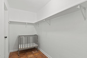 A room with a white wall, a gray crib, and a tiled floor.