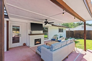 An outdoor patio with a fireplace, seating area, and a television mounted above it.