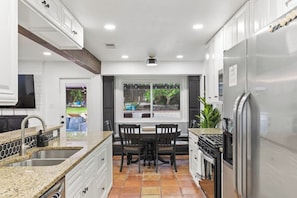 A kitchen with white cabinets, a granite countertop, a dining table with chairs, a built-in stove, and a refrigerator.
