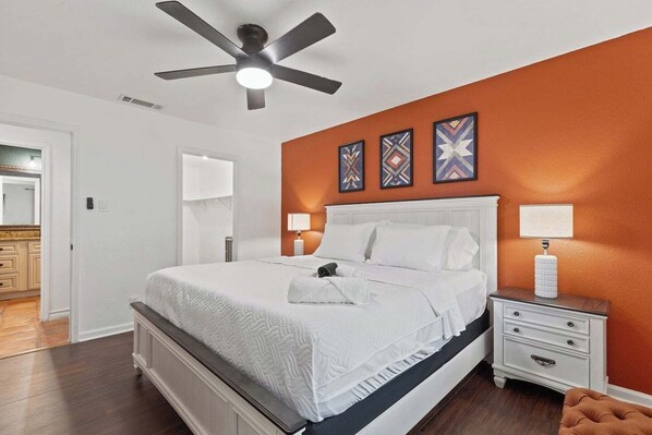 Une chambre à coucher avec un lit, des lampes de chevet, un ventilateur de plafond et des œuvres d’art décoratives au mur.