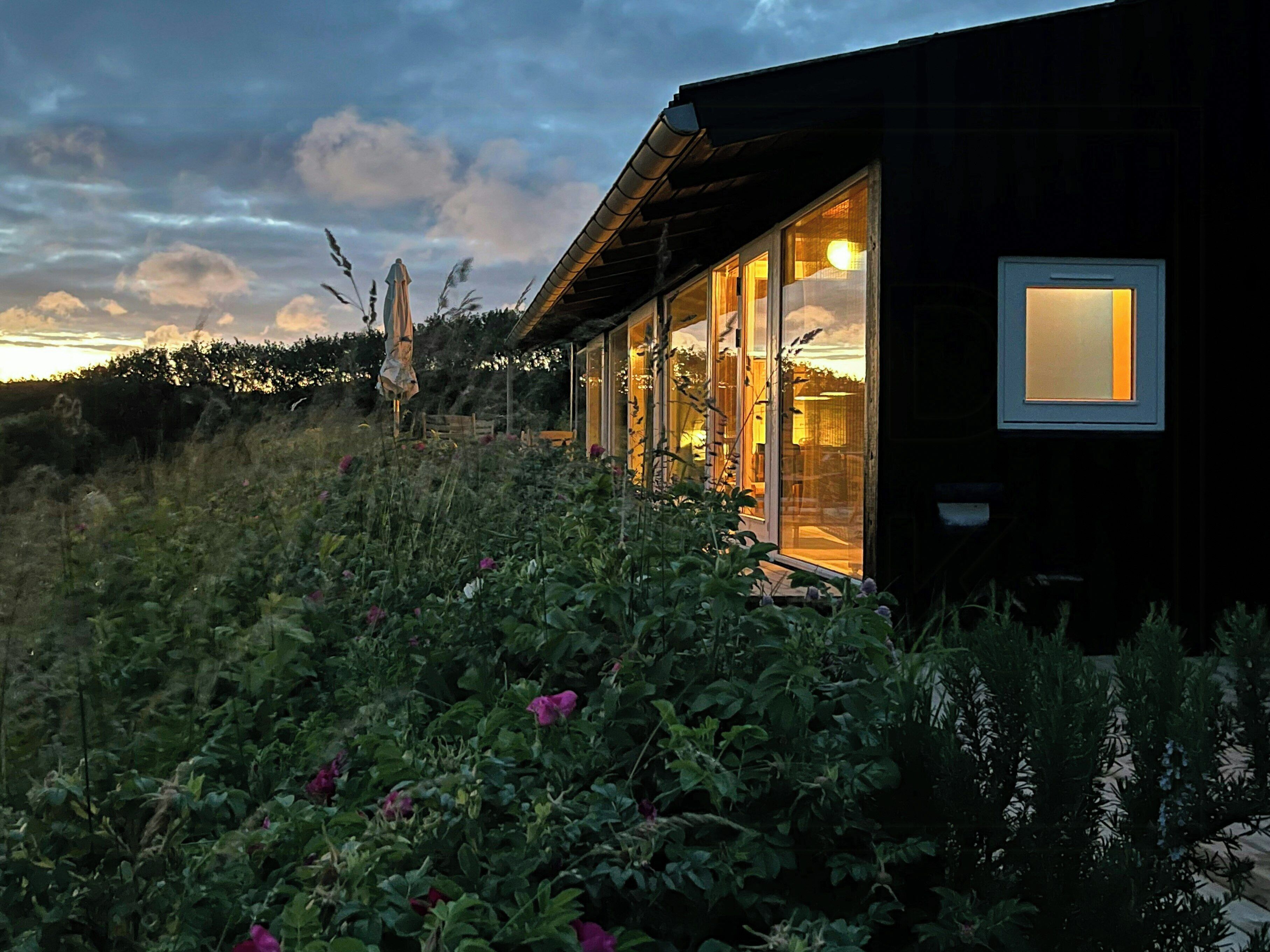 A modern house with large glass windows, a wooden deck, and a view of the sky.