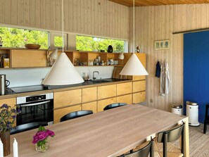 Una cucina moderna con mobili in legno, un'isola centrale, luci a sospensione e vista sul verde all'esterno.