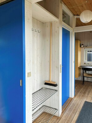 Una habitación con una puerta azul, una escoba apoyada en la pared y un estante con una rejilla metálica.