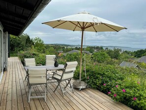 Una terraza de madera con mesa y sillas, un paraguas y vistas al paisaje.