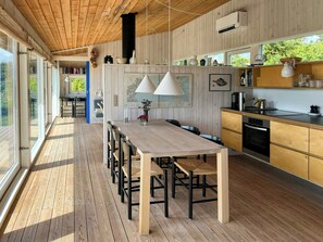 Una cucina moderna con mobili in legno, un'area pranzo con un tavolo lungo e sedie, e vista attraverso ampie finestre.