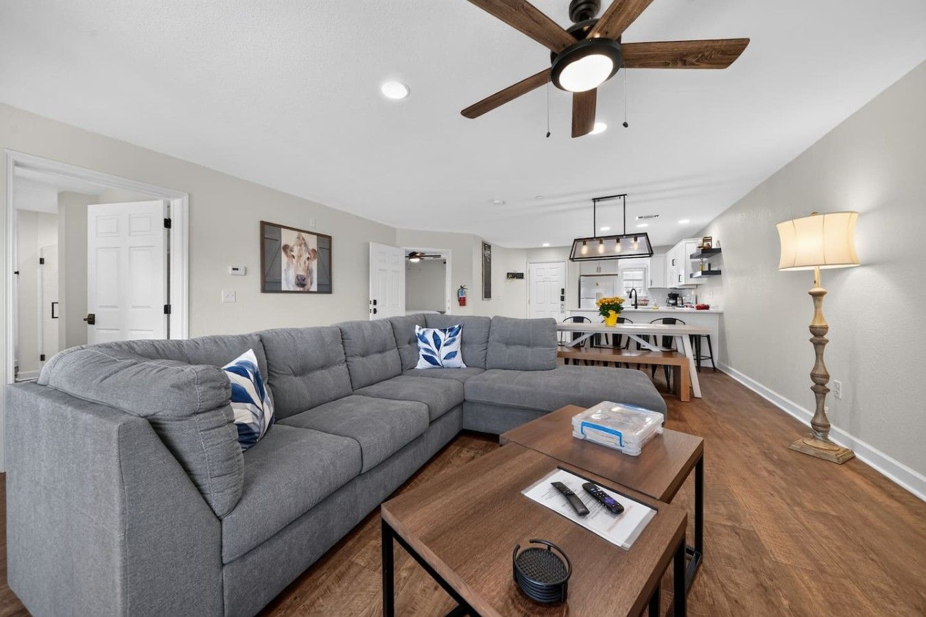 Un salon moderne avec un canapé d’angle, une table basse en bois et un ventilateur de plafond.