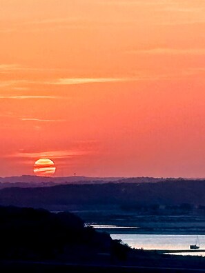 Ein Sonnenuntergang über einem Gewässer mit einer fernen Küstenlinie und einem Boot.