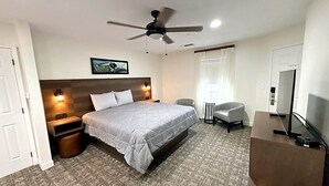 Una camera d'albergo con un letto, una scrivania, una sedia, una ventola a soffitto e una televisione.