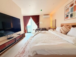 Une chambre d’hôtel avec un grand lit, un téléviseur à écran plat, un bureau et une fenêtre avec des rideaux.