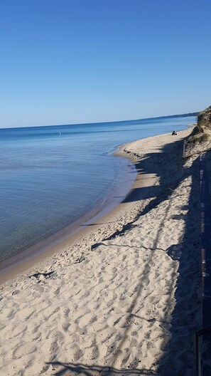 Ein Sandstrand mit klarem Wasser, ein Boot in der Ferne und eine Düne.