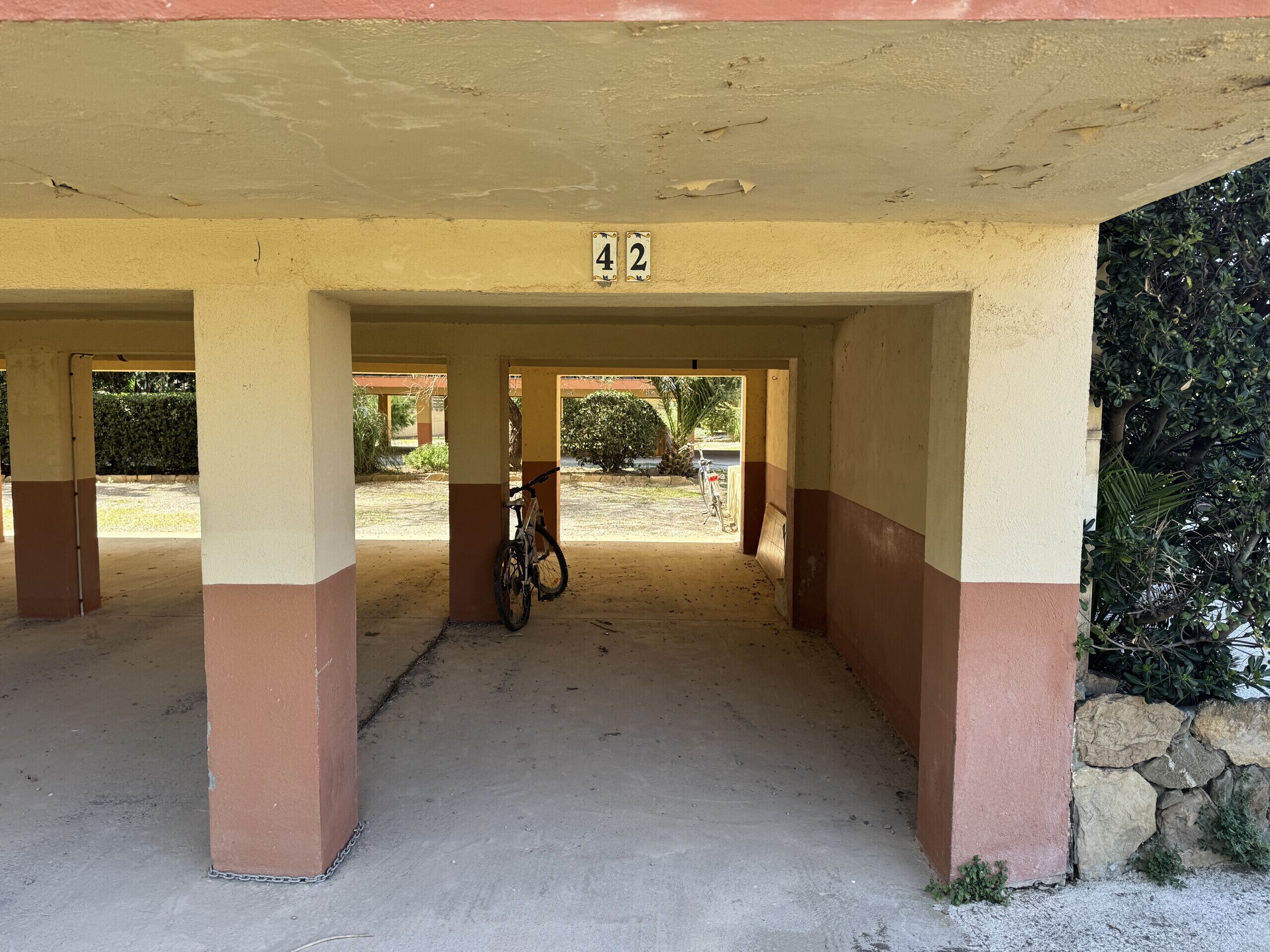 Un'area esterna coperta con pilastri numerati, una bicicletta e vista su un giardino.
