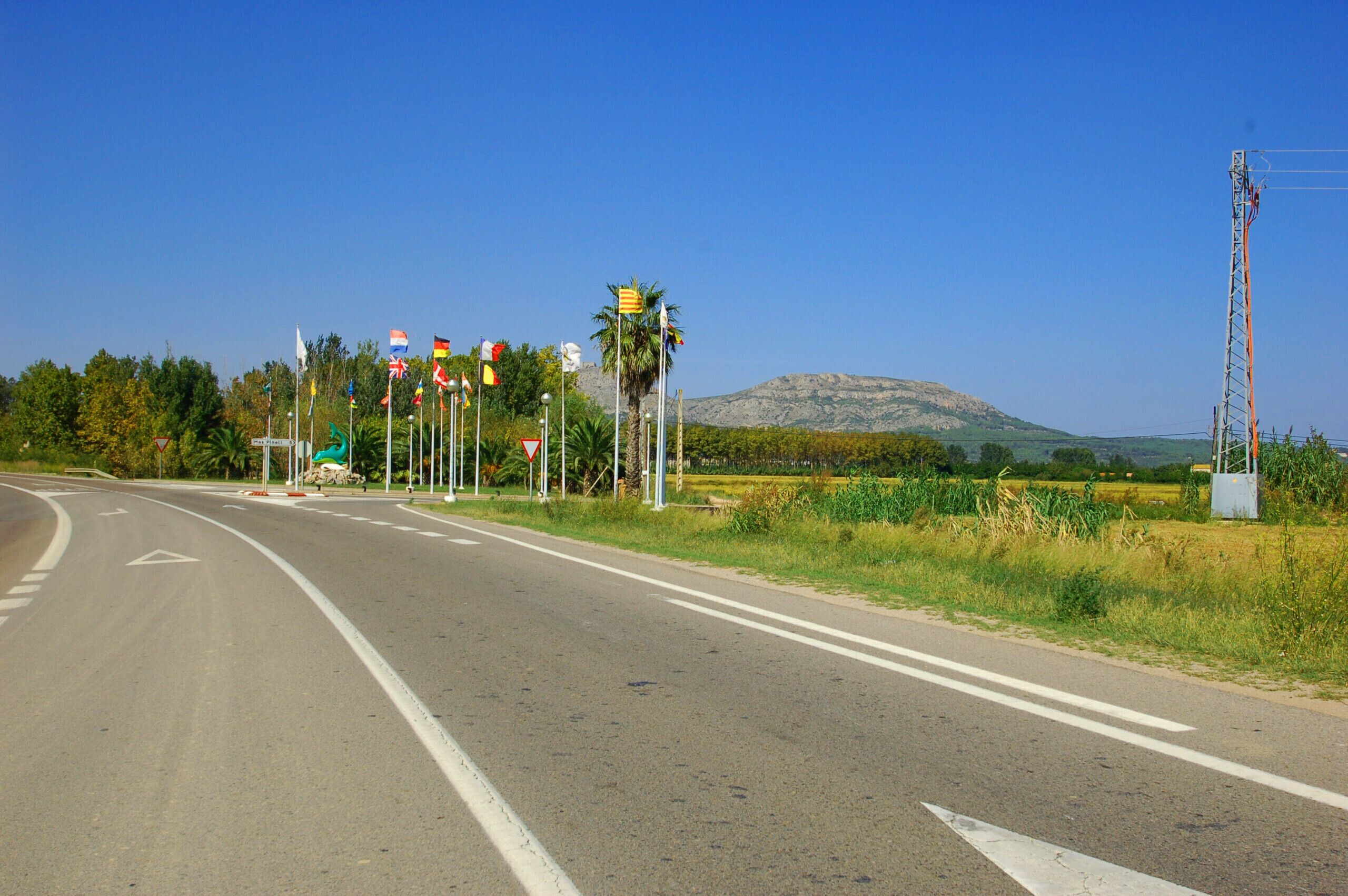 Eine Straße mit mehreren Fahrstreifen und Verkehrsschildern, umgeben von Grünflächen und einem Berg im Hintergrund.