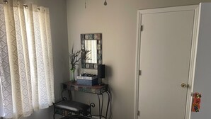 A bedroom with a bed, a bedside table with a lamp, a mirror, and a door. - Lovely 2-bed 2-bath house with firepit in fenced in yard in charming Youngsville (Youngsville)