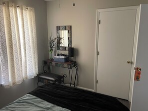 Ein Schlafzimmer mit Bett, Nachttisch mit Lampe, Spiegel und Tür.