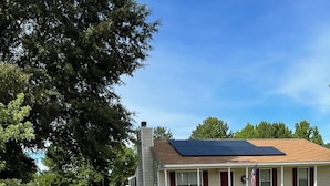 A residential house with a solar panel, a front porch, and a small shed in the background. - Lovely 2-bed 2-bath house with firepit in fenced in yard in charming Youngsville (Youngsville)