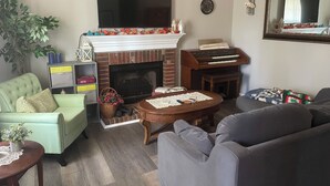 A living room with a fireplace, a television, a sofa, a coffee table, and a bookshelf. - Lovely 2-bed 2-bath house with firepit in fenced in yard in charming Youngsville (Youngsville)