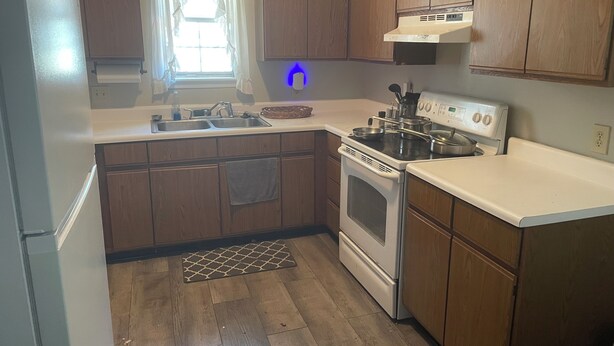 A kitchen with wooden cabinets, a stainless steel sink, a stove, and a window with curtains. - Lovely 2-bed 2-bath house with firepit in fenced in yard in charming Youngsville (Youngsville)
