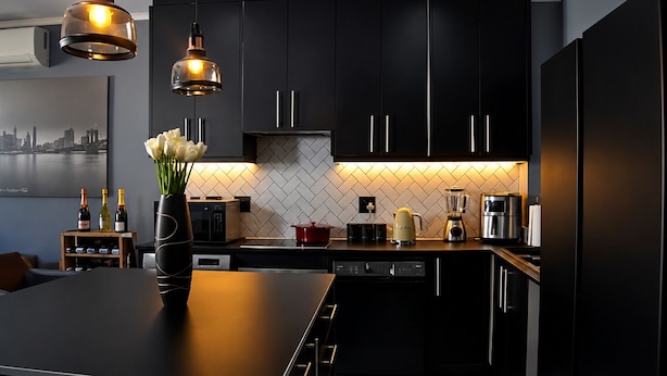 Une cuisine moderne avec des meubles de couleur sombre, un îlot central et des luminaires suspendus.