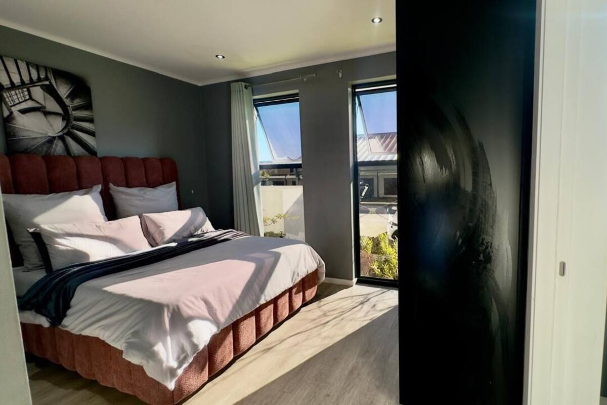 Ein modernes Schlafzimmer mit einem großen Bett, Blick ins Freie und einer schwarzen Tür.