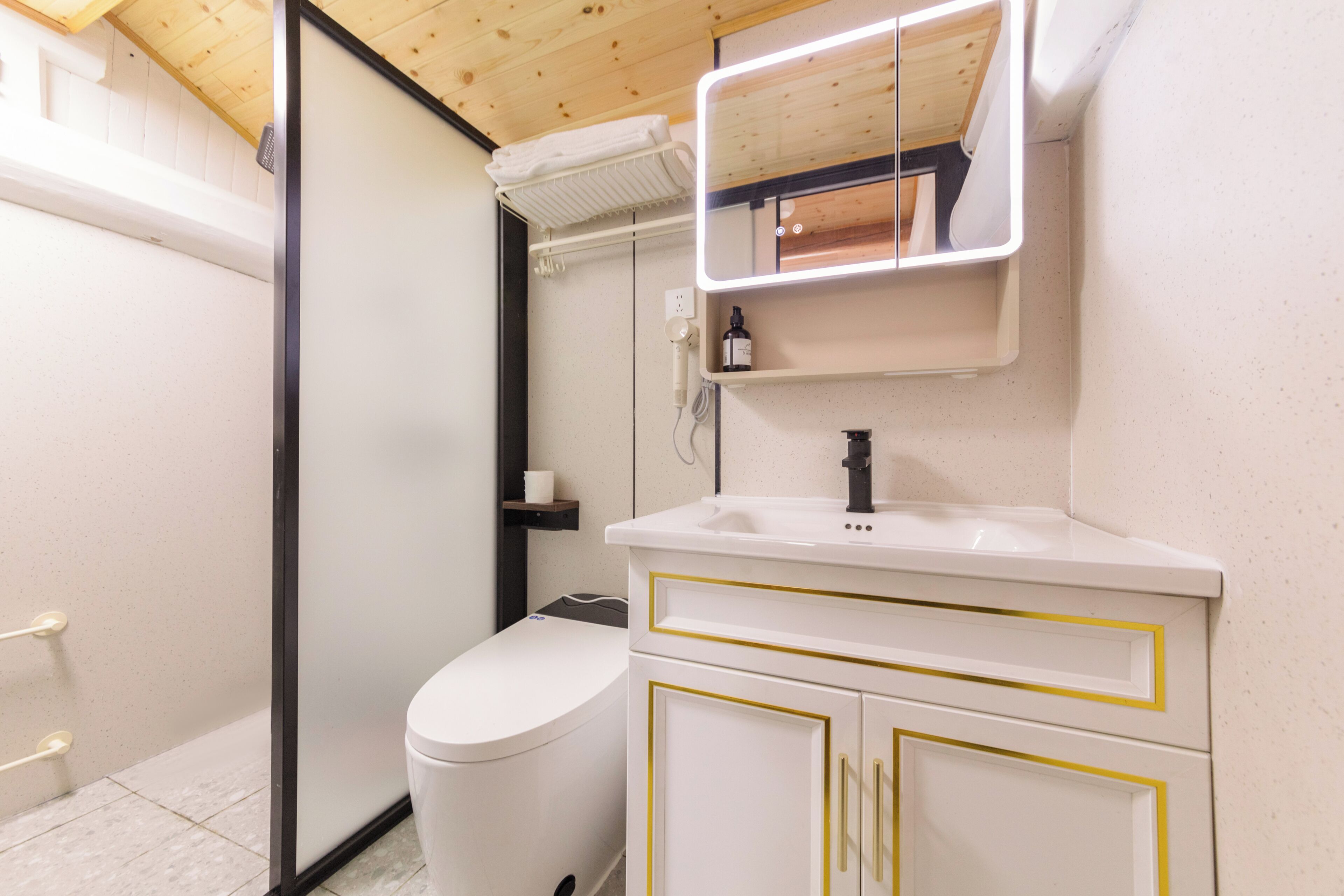 Un baño con inodoro, lavamanos con detalles dorados, espejo y toallero.