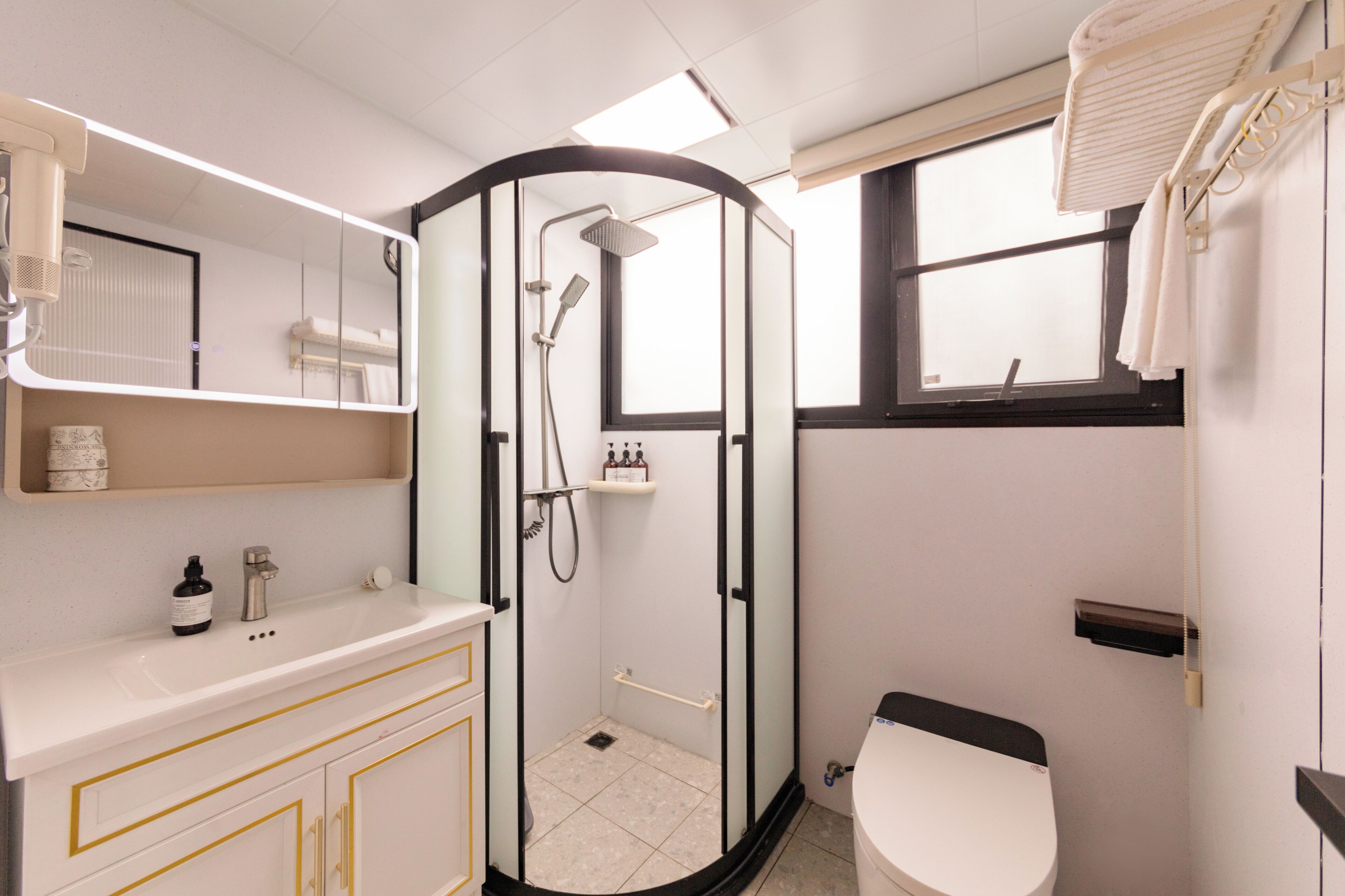 Un baño con ducha de mampara de vidrio, lavabo blanco con detalles dorados y retrete.