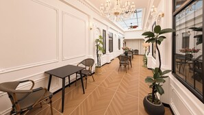 A spacious room with a high ceiling, a chandelier, a dining area with tables and chairs, and large windows. - Le Qin Courtyard Hotel (Beijing)