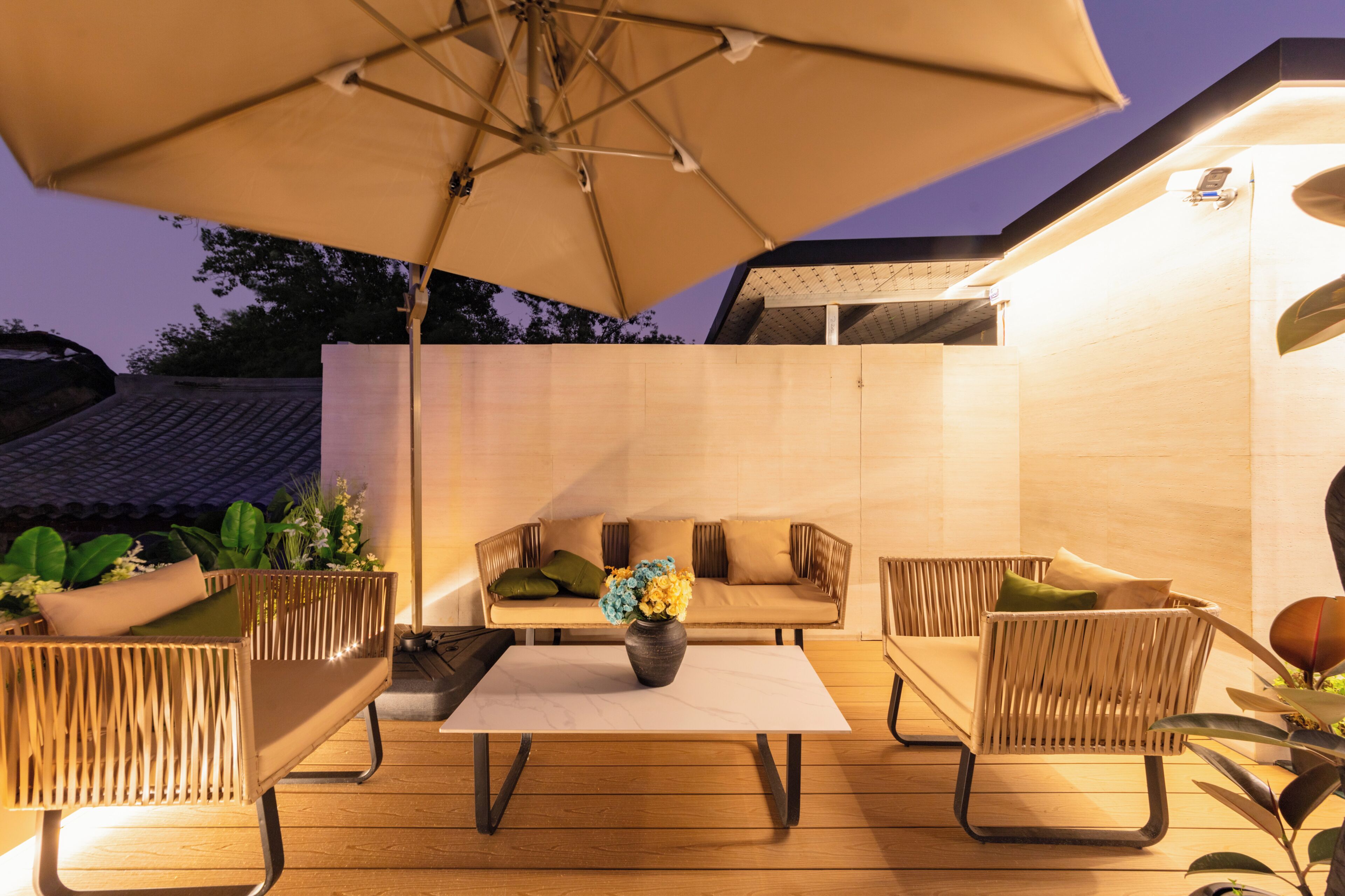 Een terras buiten met een bank, stoelen, een tafel en een parasol.