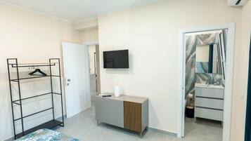 A bedroom with a bed, a wardrobe, a TV, and a bathroom with a mirror and sink.