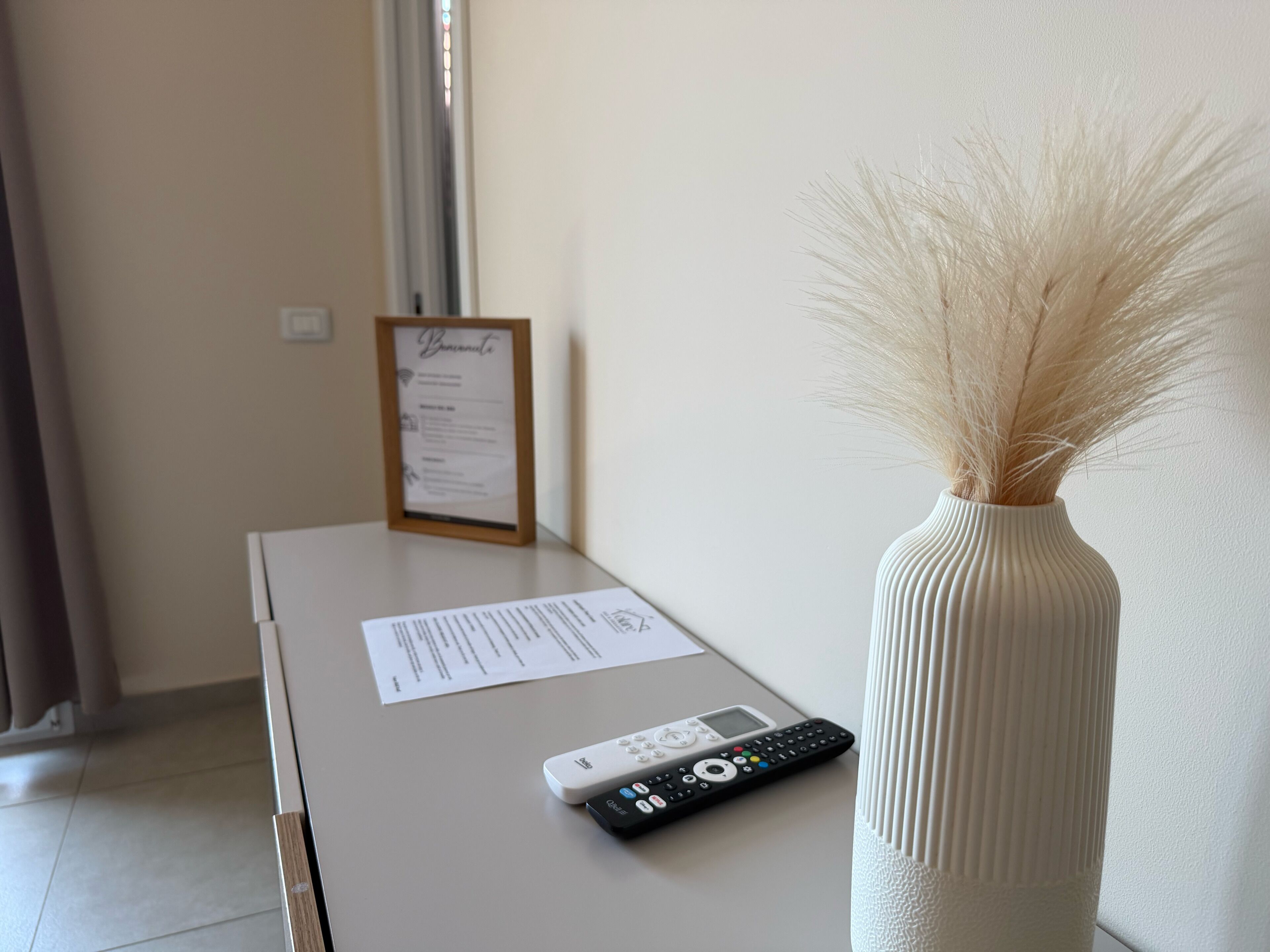 Une chambre d’hôtel équipée d’un bureau, d’une télécommande, d’un menu encadré et d’un vase contenant des herbes de la pampa séchées.