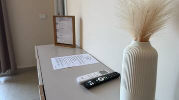 Une chambre d’hôtel équipée d’un bureau, d’une télécommande, d’un menu encadré et d’un vase contenant des herbes de la pampa séchées.