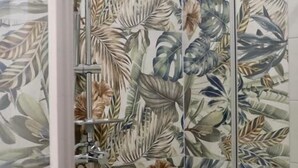 A shower enclosure with a tropical leaf pattern wallpaper.