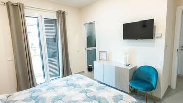 Un dormitorio con cama, televisor montado en la pared, escritorio, silla y puerta corredera.