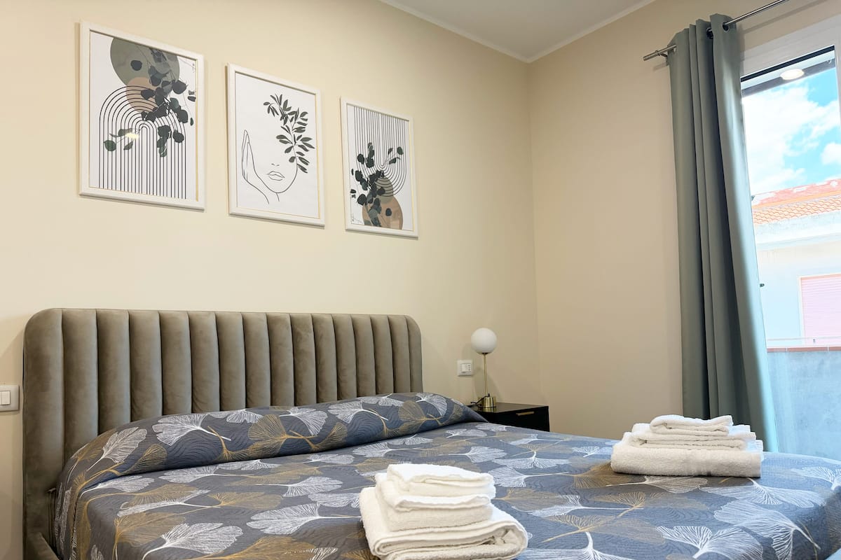 A neatly made bed with a patterned bedspread, a bedside lamp, and three framed artworks on the wall.