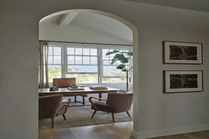 Ein Zimmer mit Schreibtisch, zwei Stühlen, einem großen Fenster und zwei gerahmten Bildern an der Wand.