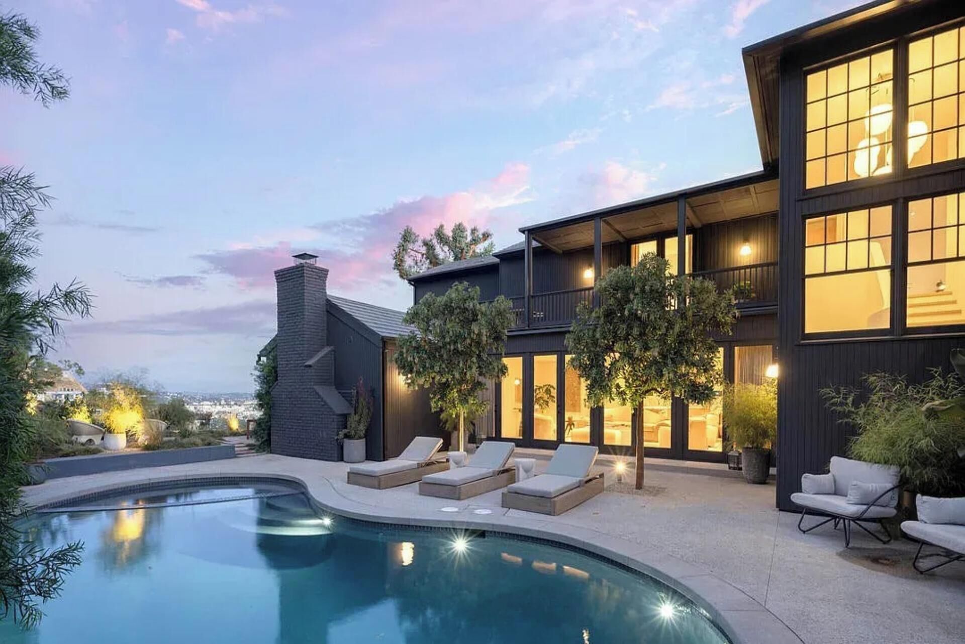 A modern house with a swimming pool, lounge chairs, and a large windowed balcony.