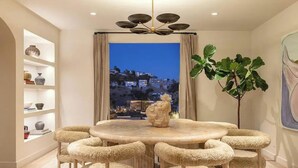 A dining area with a round table, six chairs, a chandelier, a view of a cityscape, and a large plant. - Sunset Manor - Designer Gated Estate Above Sunset Strip | Panoramic LA Views (Los Angeles)