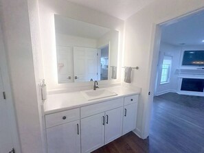 Un baño con tocador blanco, un espejo grande y un lavamanos.