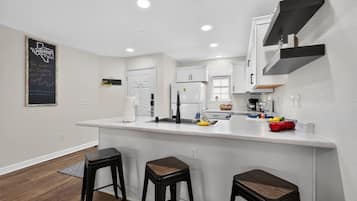 A modern kitchen with a white countertop, black stools, and a chalkboard sign.