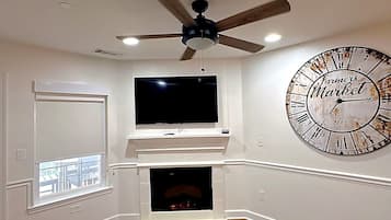A room with a fireplace, a large wall clock, and a ceiling fan.