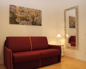 Ein rotes Sofa, ein kleiner Tisch mit einer Lampe, ein großer Spiegel und ein Blumenbild an der Wand.