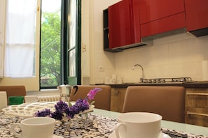 Eine moderne Küche mit roten Schränken, einem Esstisch mit weißen Tassen und einer Vase mit lila Blumen, mit Blick auf Grünfläche.