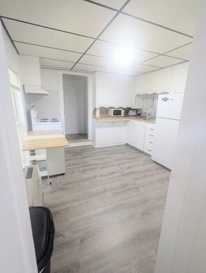 Una cocina compacta con armarios blancos, microondas, estufa y encimera de madera.