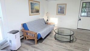 Een kamer met een bed, een kachel, een glazen salontafel en twee ingelijste foto's aan de muur.