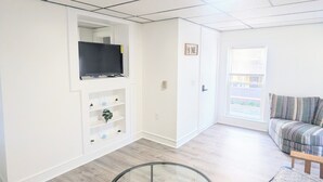 Een moderne woonkamer met een glazen tafel, een bank, een televisie op een plank en een raam met zonwering.