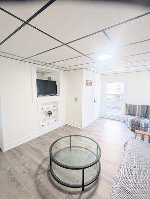 Een moderne woonkamer met een glazen tafel, een bank, een televisie op een plank en een raam met zonwering.