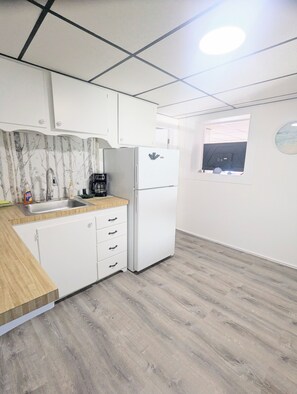 Una cocina con armarios blancos, un fregadero, un refrigerador y una cafetera.