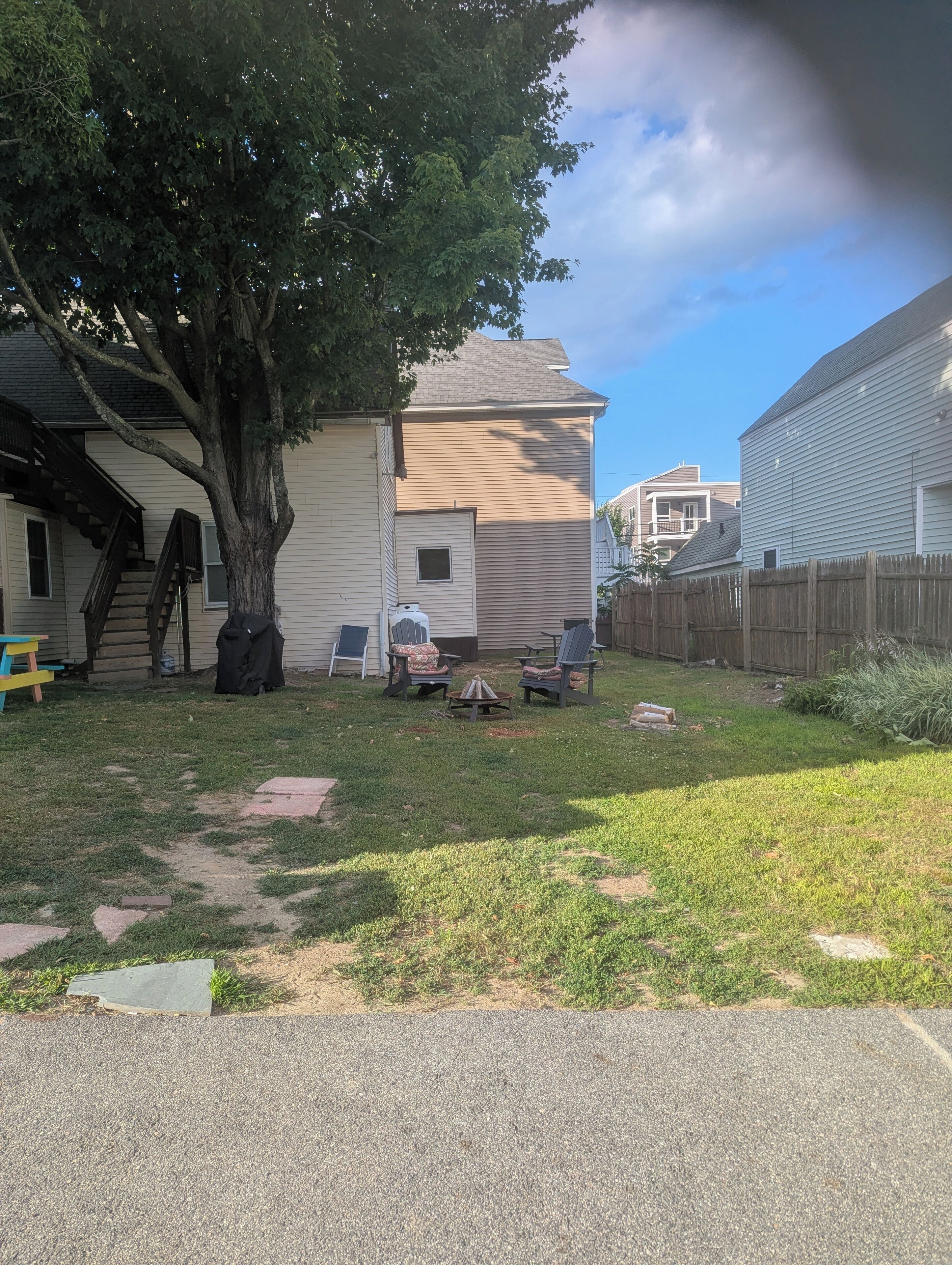 A residential backyard with a tree, a barbecue grill, and outdoor seating.