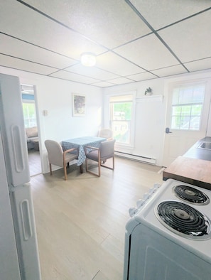 A compact kitchen with a stove, a dining table with chairs, and a door leading to a balcony. - newly updated, pet friendly, located in a quiet neighborhood, 10 minute walk to the beach (old orchard beach)