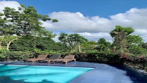 Una piscina con sillas de descanso, rodeada de abundante vegetación y árboles.